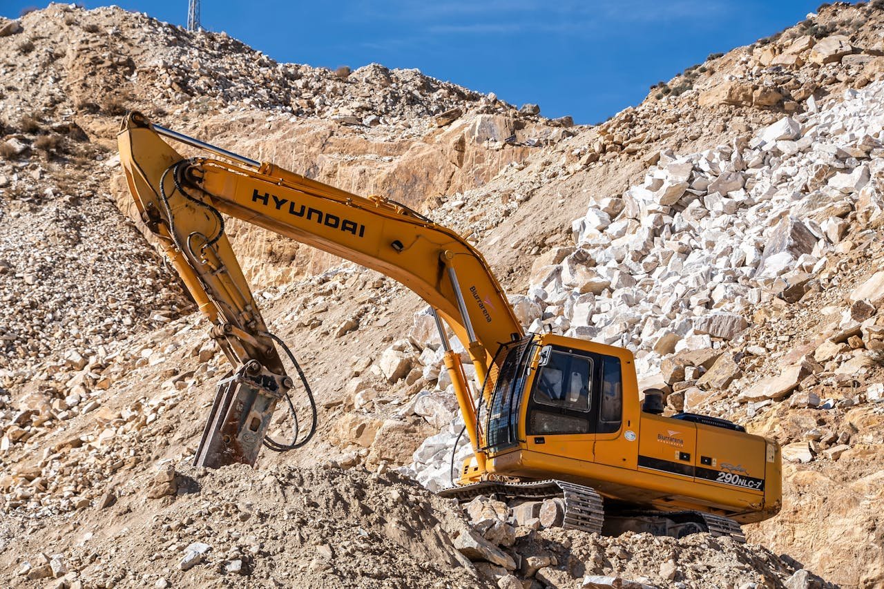 Yellow Hyundai excavator operating in a rocky quarry under a clear blue sky. Perfect for industrial themes.
